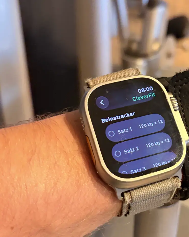 Apple Watch am Handgelenk an der Maschine: die Satzliste des heutigen Trainings in LeibFit – Beinstrecker, drei Sätze à 120 kg × 12, jeder direkt am Arm abhakbar